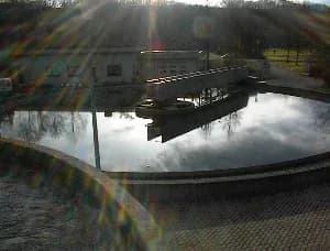 Rundes Klärbecken einer Kläranlage mit Brücke und Betriebsgebäude im Hintergrund